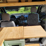 Spacious rv rental interior: wooden tables in foreground, leading to driver's cabin and dashboard.