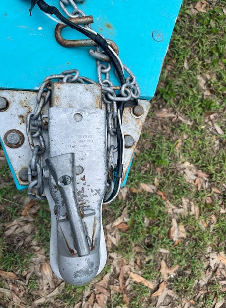 RV rental trailer connection: coupler, safety chains, and wiring on a blue tongue, viewed from above.