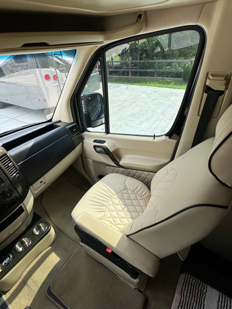 Comfy RV rental interior: cream quilted passenger seat, dashboard, and view out the window of another RV. — photo 15