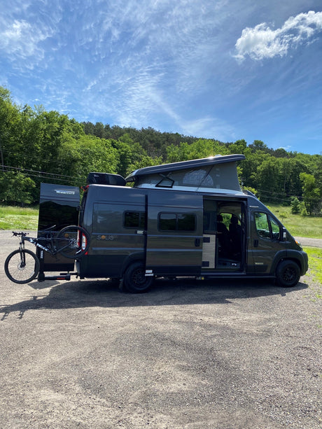 Dark grey Winnebago Solis RV rental parked outdoors, with raised pop-top, open side door, and bike rack.