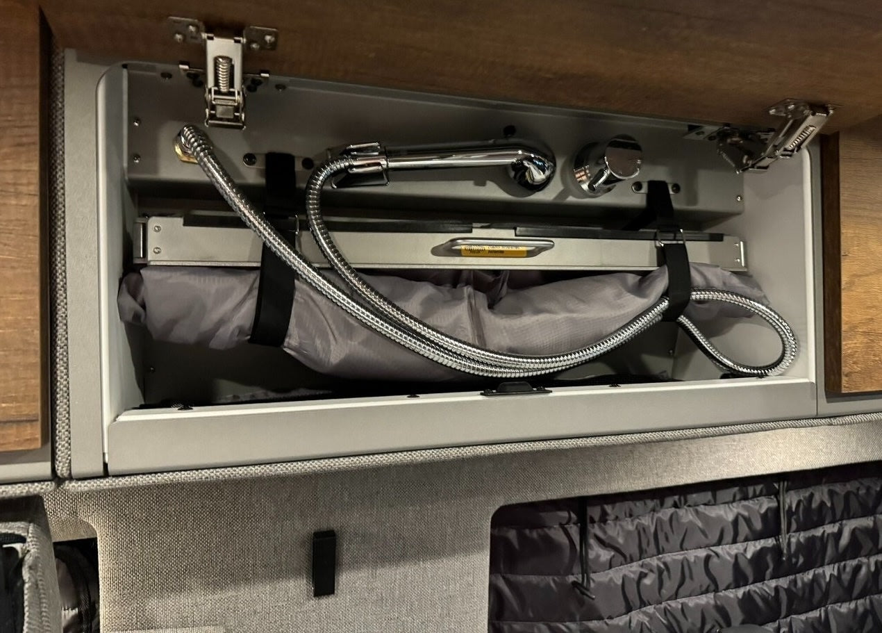 Compact RV rental shower with flexible hose, shower head, and controls, neatly stowed above a folded basin for space-saving.