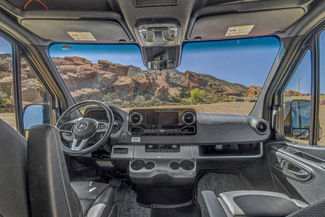 RV rental camper van interior with Mercedes dashboard, steering wheel, and seats, viewing a scenic rocky landscape.