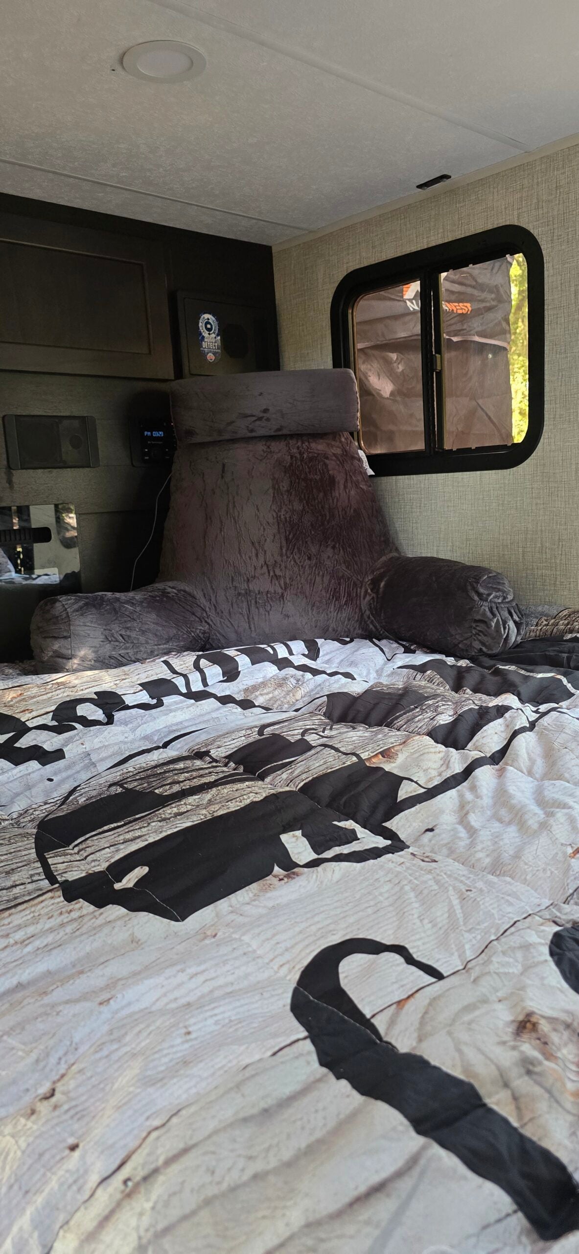 Relaxing RV rental bedroom: A bed with a wood-patterned duvet, a soft gray backrest pillow, and a small window view.