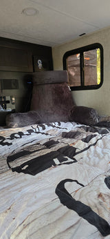 Relaxing RV rental bedroom: A bed with a wood-patterned duvet, a soft gray backrest pillow, and a small window view.