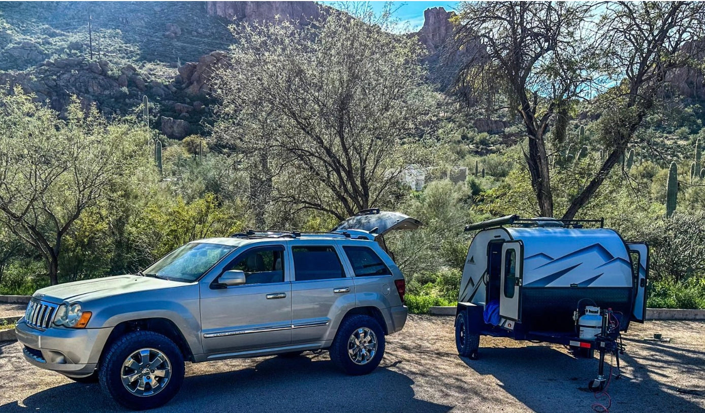 Explore the great outdoors with this RV rental setup: a silver Jeep SUV & teardrop camper in a desert landscape. Mountains visible. #rvrental