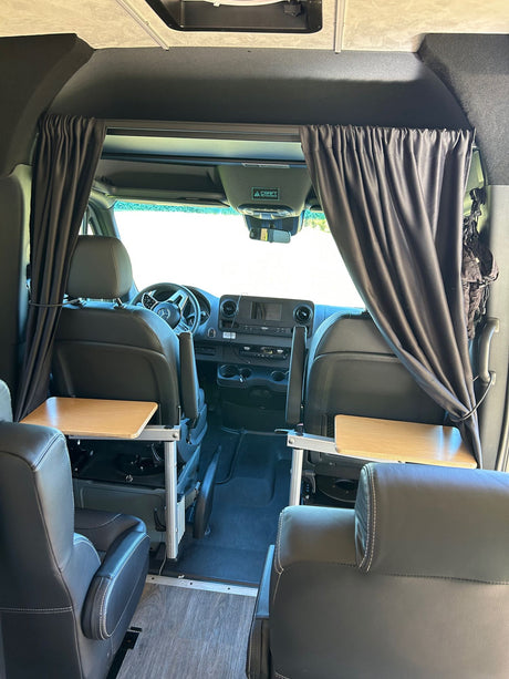 Spacious Mercedes Sprinter RV rental interior with swivel seats, portable tables, and privacy curtains, perfect for travel.