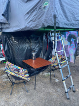 Rooftop tent setup for RV rental: NOMADIC tent, lower annex, portable table with lantern, chairs, and ladder for a cozy camp.