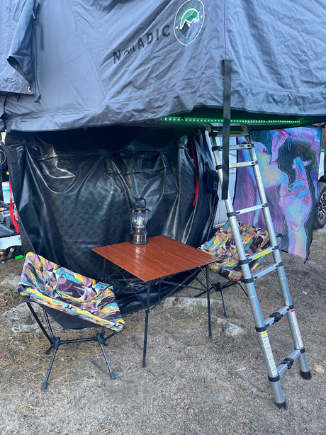 Rooftop tent setup for RV rental: NOMADIC tent, lower annex, portable table with lantern, chairs, and ladder for a cozy camp.