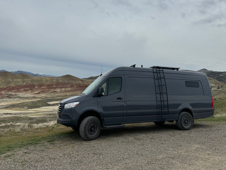Adventure awaits! This gray camper van, perfect for an RV rental, explores colorful hills under an overcast sky.