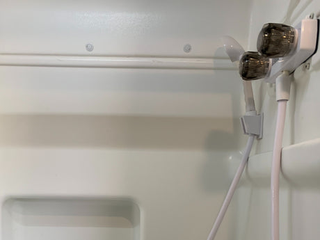 An RV rental's white, molded shower stall interior featuring a two-knob faucet and attached handheld shower head.