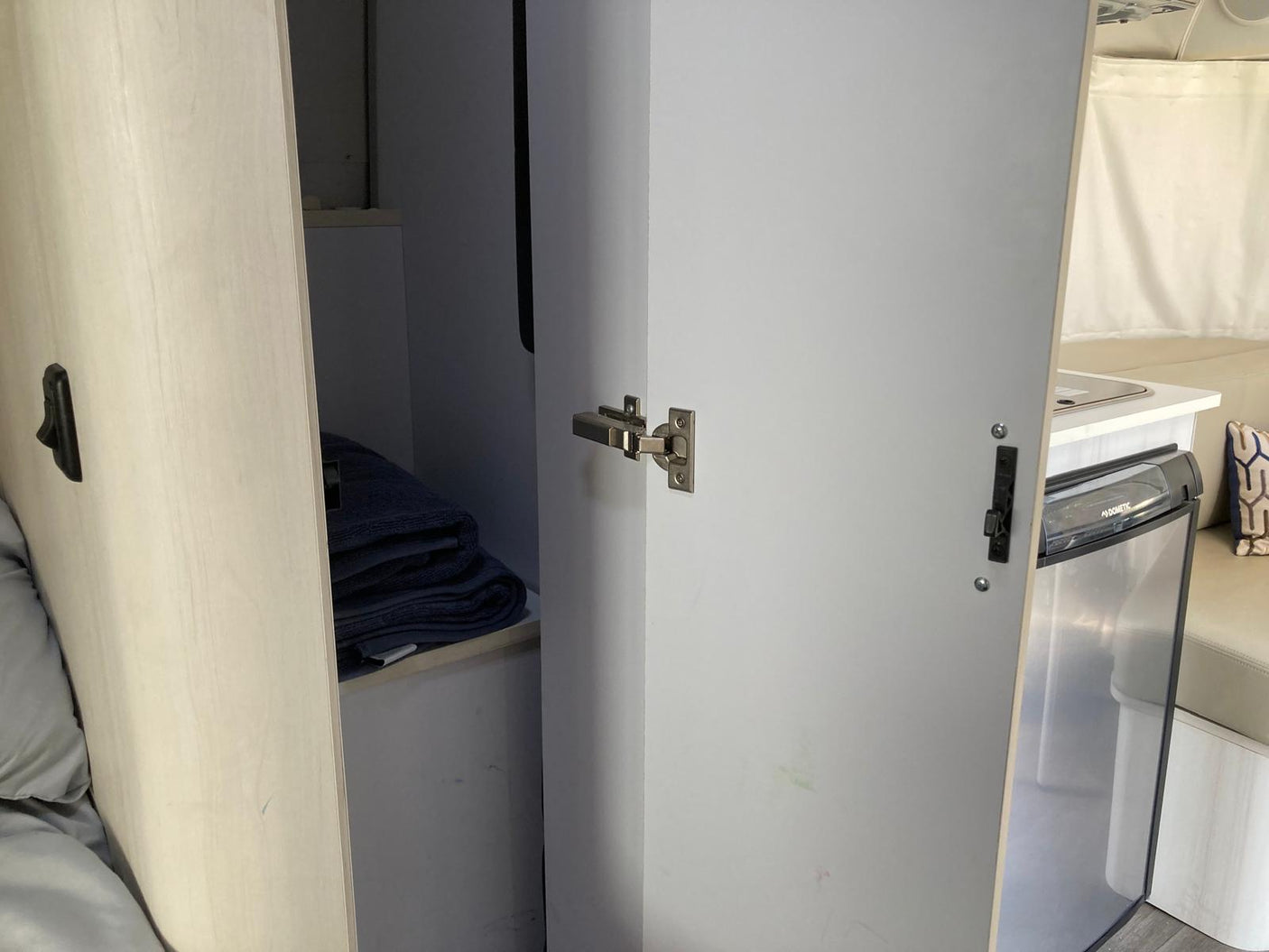 Inside an RV rental: storage cabinet with towels and a Dometic fridge in a compact kitchen area, highlighting efficient design.