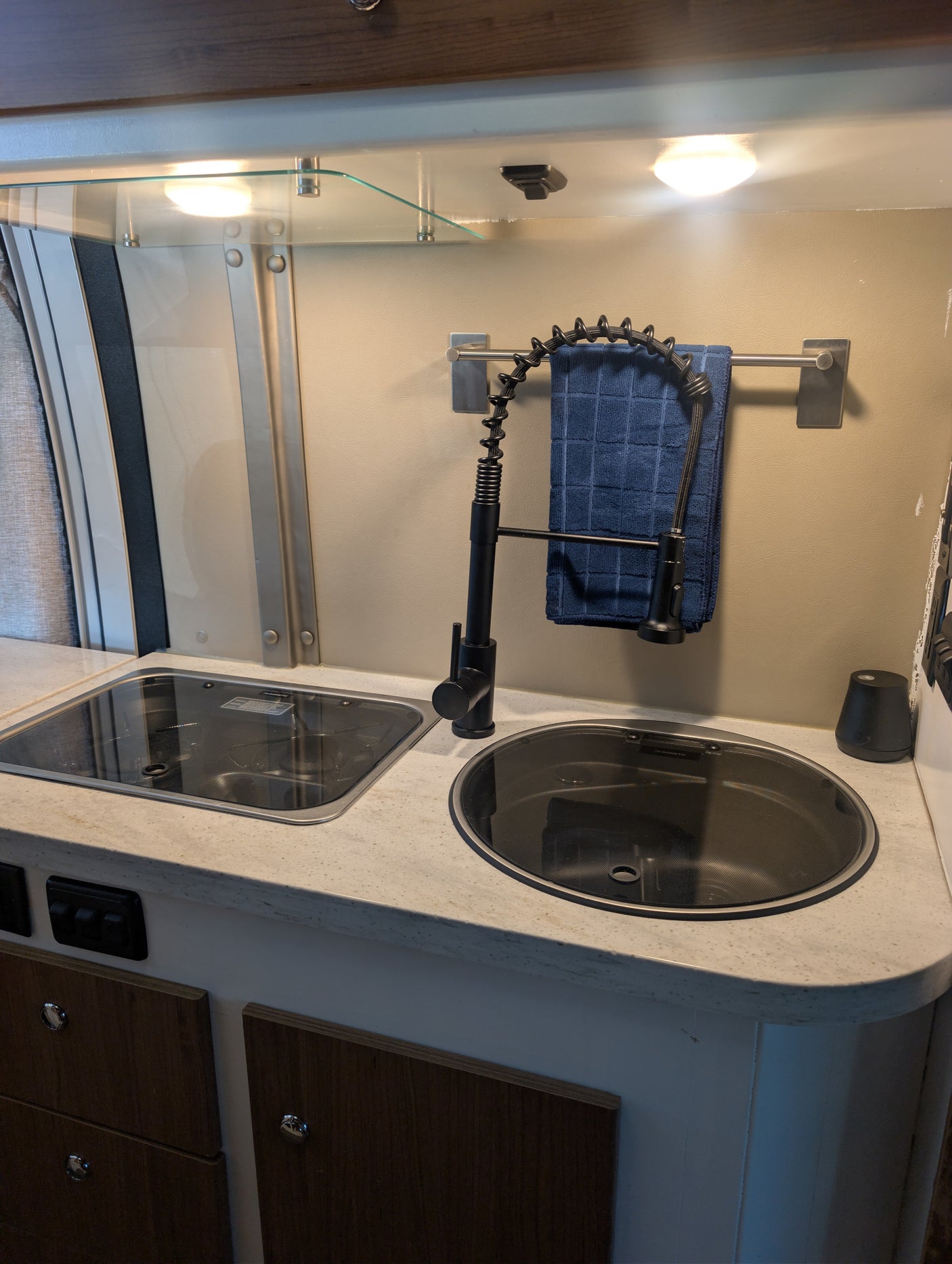 Compact rv rental kitchen with an integrated stovetop, sink, pull-down faucet, under-cabinet lighting, and wooden storage.