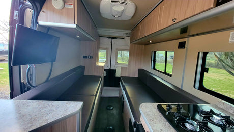 Spacious RV rental interior with convertible seating, kitchen, and TV. This camper van offers a comfortable living space for travel.