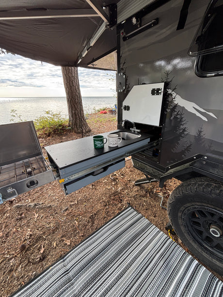 RV rental: outdoor kitchen (sink, stove) extended from a travel trailer, by a lake. Camping with a view!
