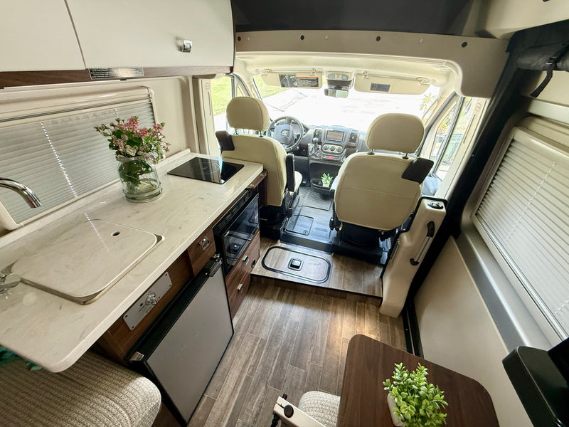 Interior of a modern rv rental: shows kitchen counter with sink & stove, fridge, wood flooring, and driver's cabin. — photo 2