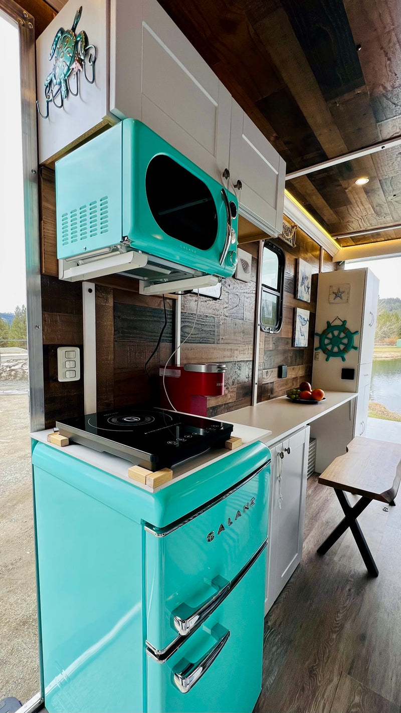 This compact RV rental kitchen boasts a retro teal Galanz fridge, microwave, and induction cooktop, offering scenic pond views. — photo 10