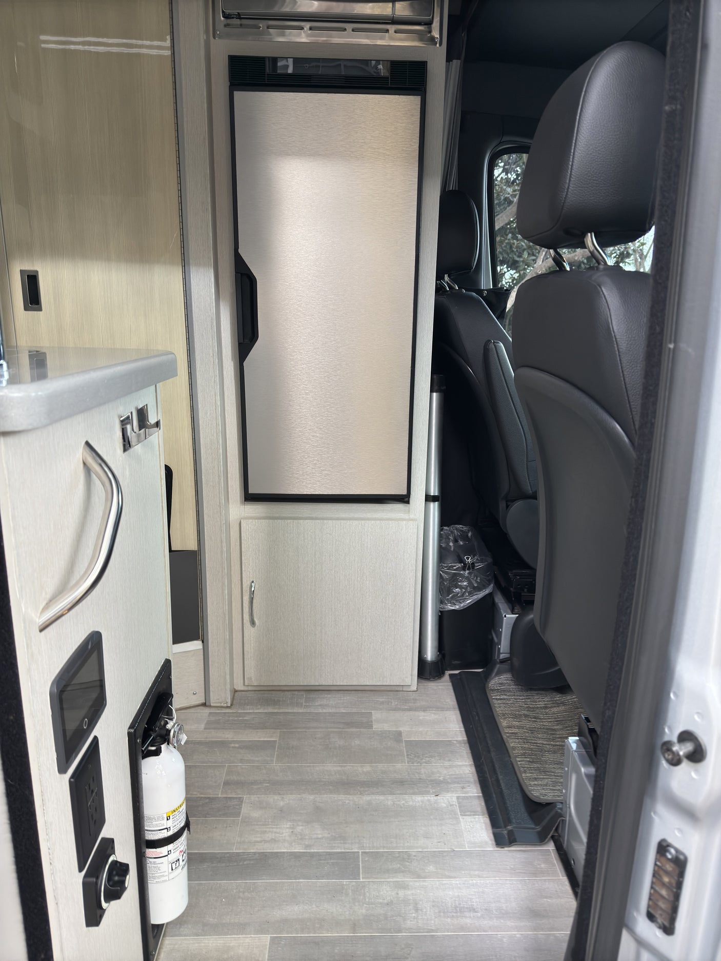 RV rental interior: kitchenette, refrigerator, fire extinguisher, and front passenger seats. Compact, functional design.