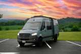 Grey Mercedes Sprinter RV rental with roof rack & ladder, parked in a scenic landscape at sunset.