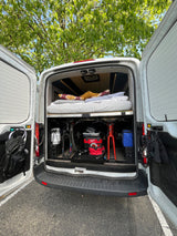 Inside an rv rental: Cozy bed above organized storage for two bikes, propane, tools, and outdoor essentials.