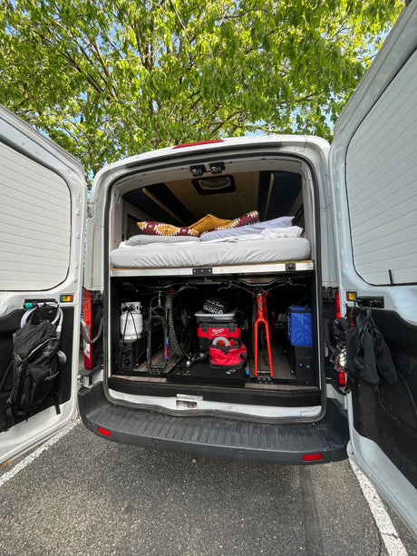 Inside an rv rental: Cozy bed above organized storage for two bikes, propane, tools, and outdoor essentials.