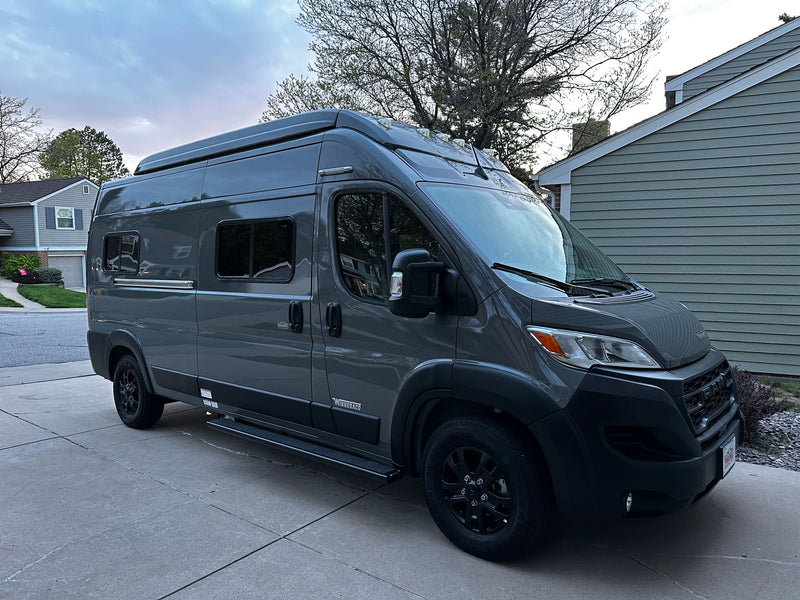  in a scenic mountain landscape under a dramatic sky.|Grey pop-top camper van RV rental parked in a driveway. Side door open reveals interior. House and trees in background.|Modern gray Winnebago camper van — photo 3