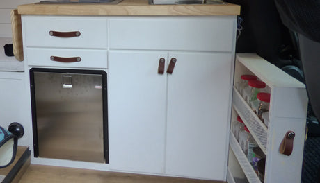 RV rental kitchen: compact white cabinets with leather pulls, built-in mini-fridge, and pull-out spice rack.