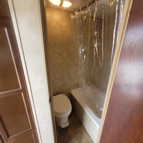 RV rental bathroom with a toilet on the left and a bathtub/shower with a clear curtain on the right, lit by an overhead fixture.