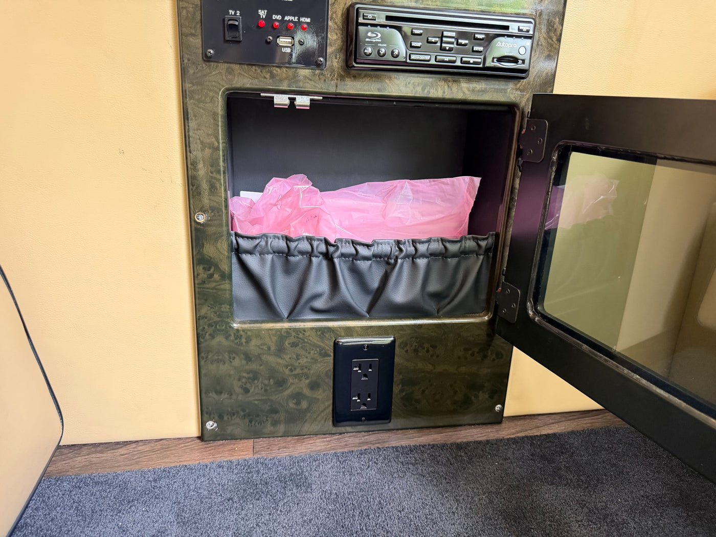 RV rental interior featuring a media control panel, Blu-ray player, an open storage compartment with a pink bag, and a power outlet. — photo 20