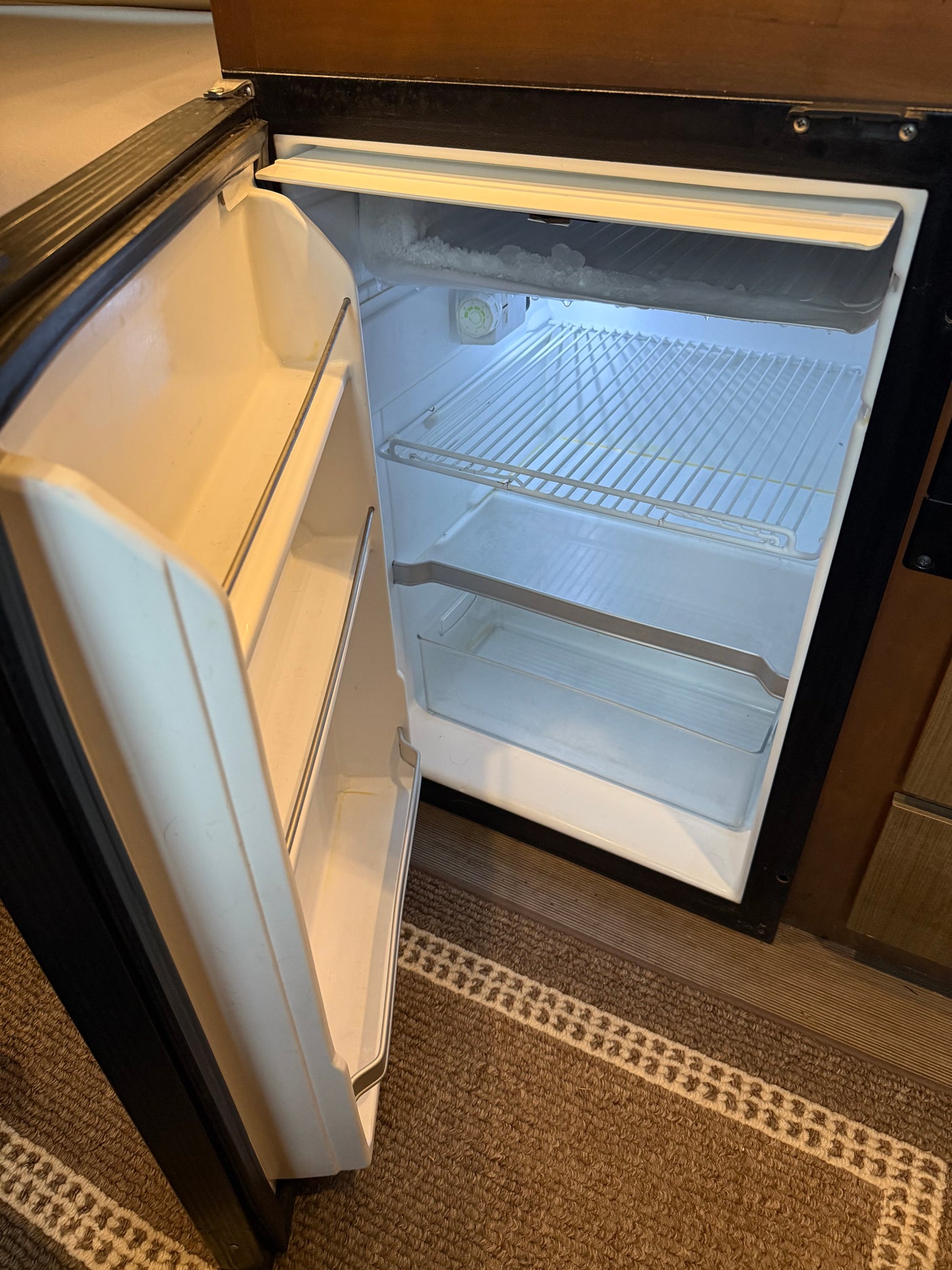 RV rental mini-fridge, open and empty. Visible frost in the top freezer section. Compact refrigerator with interior wire shelves.
