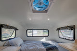 The bright interior of an RV rental, showing a comfortable bed, multiple windows, a ceiling fan, and practical counter space.