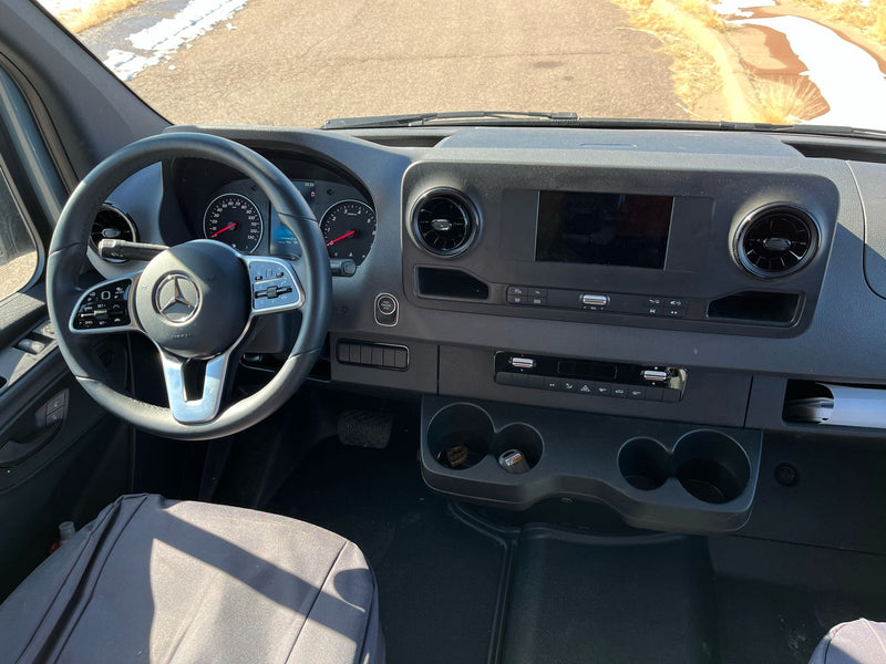  parked by dry fields with distant mountains under a clear blue sky.|An rv rental's rooftop showing solar panels & a large AC/ventilation unit against a scenic mountain backdrop.|Interior view of an RV rental camper van with open back doors — photo 10
