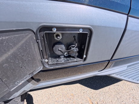 RV rental: Open utility panel on grey van showing water fill cap and other connections for camper services.