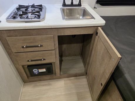 RV rental: Compact kitchenette with a two-burner stove, sink, and wood-grain cabinets offering storage, including a small safe.