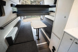 RV rental campervan interior: dining area with benches, a central table, and an overhead bunk bed, ready for travel.