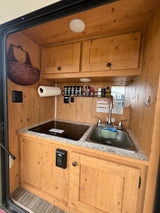 Detailed view of an RV rental's cozy wood-paneled kitchenette with sink, Dometic cooktop, and spice rack.