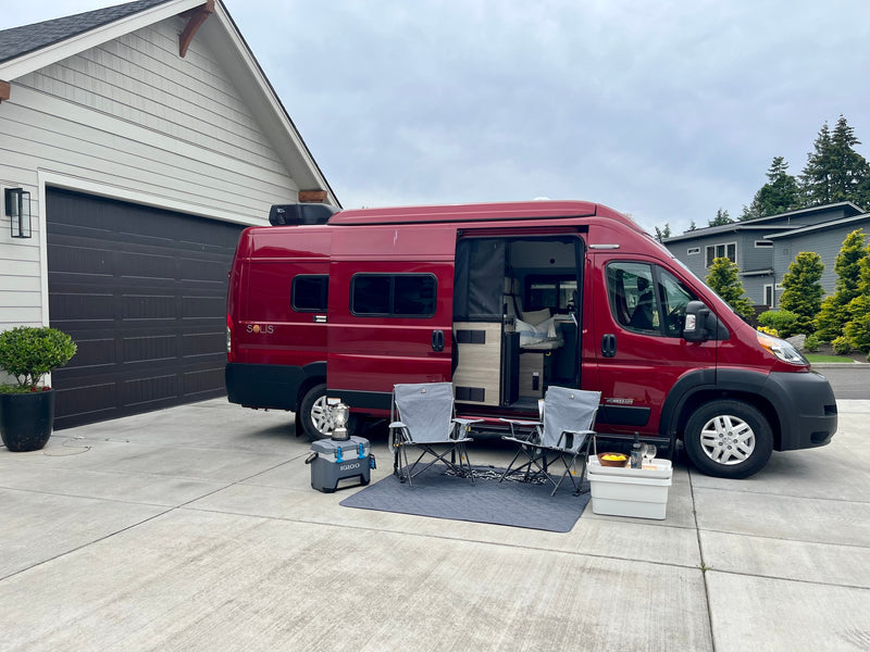 Relaxing by a red Winnebago Solis rv rental: a cozy outdoor setup with chairs, cooler, and open camper van door in a driveway. — photo 11
