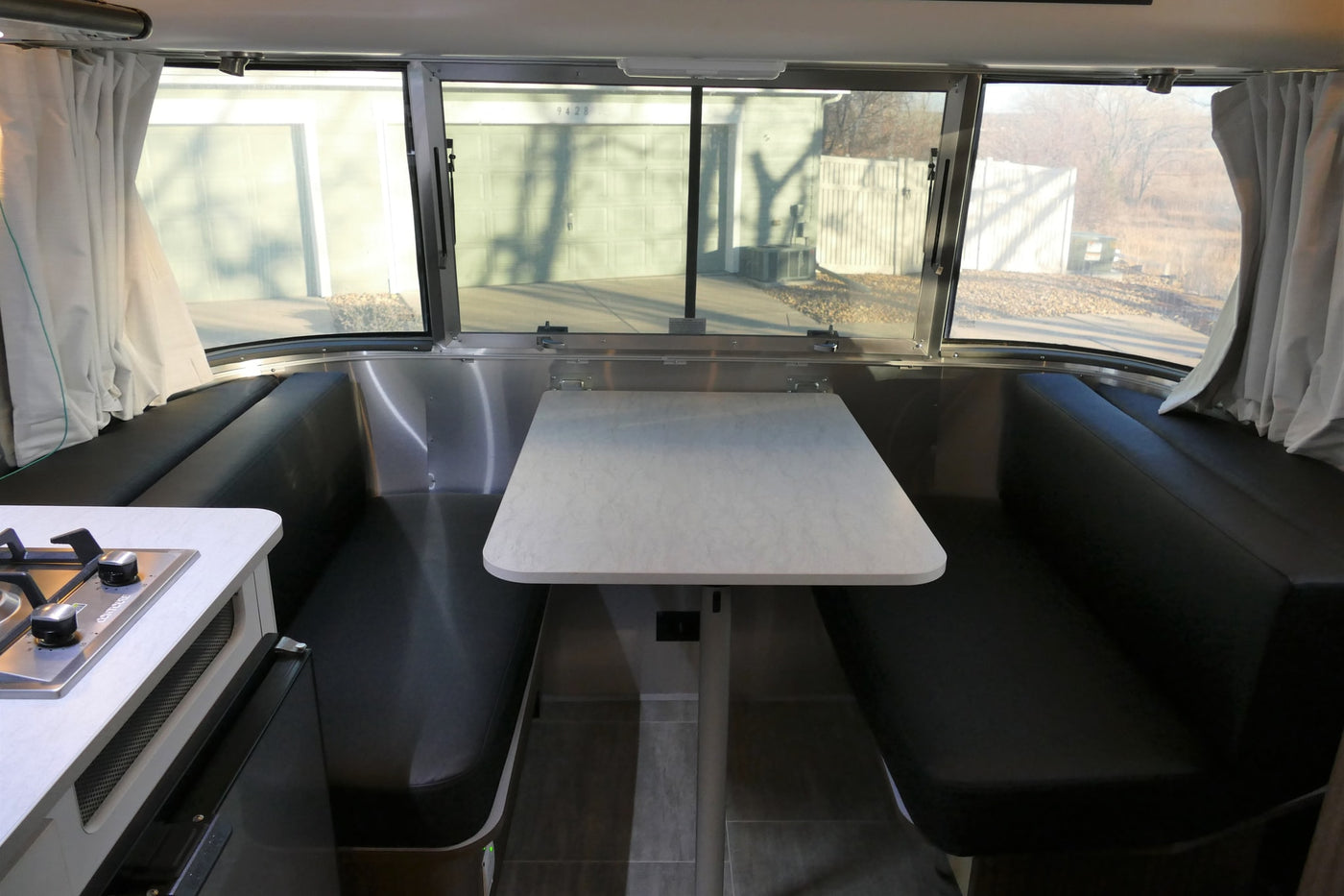 RV rental: Bright interior of a travel trailer, featuring a modern dinette with black benches, a white table, and a kitchen stove. — photo 16