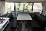 RV rental: Bright interior of a travel trailer, featuring a modern dinette with black benches, a white table, and a kitchen stove.