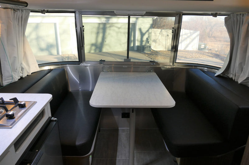 RV rental: Bright interior of a travel trailer, featuring a modern dinette with black benches, a white table, and a kitchen stove. — photo 16
