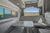 RV rental's inviting dinette with gray seating, table, and a picturesque view of hills and water from large windows.