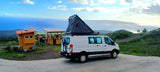 RV rental van with rooftop tent at a scenic overlook near a roadside eatery, offering stunning ocean and mountain views.