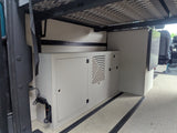 RV rental interior: Organized storage, cabinet with vent, and refrigerator under a bed frame in a camper van.