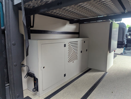 RV rental interior: Organized storage, cabinet with vent, and refrigerator under a bed frame in a camper van.