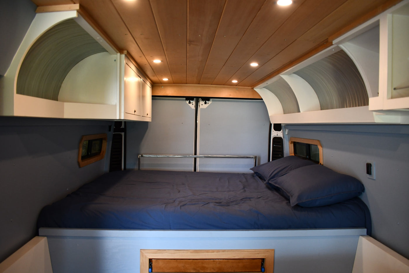 This RV rental features a comfortable sleeping area with a dark blue bed, bright wood ceiling, and built-in overhead storage. — photo 8