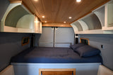 This RV rental features a comfortable sleeping area with a dark blue bed, bright wood ceiling, and built-in overhead storage.