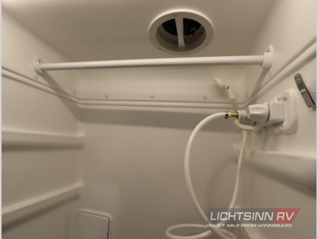 Inside a compact RV rental shower: white interior, hose, shower head, overhead vent, and built-in storage shelves.