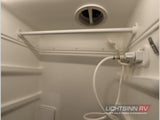 Inside a compact RV rental shower: white interior, hose, shower head, overhead vent, and built-in storage shelves.