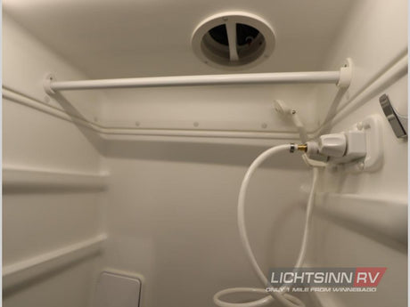 Inside a compact RV rental shower: white interior, hose, shower head, overhead vent, and built-in storage shelves.