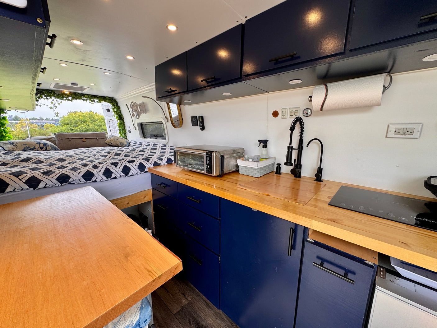 Cozy RV rental interior with a well-equipped kitchenette featuring blue cabinets, wood countertops, and a comfortable bed.