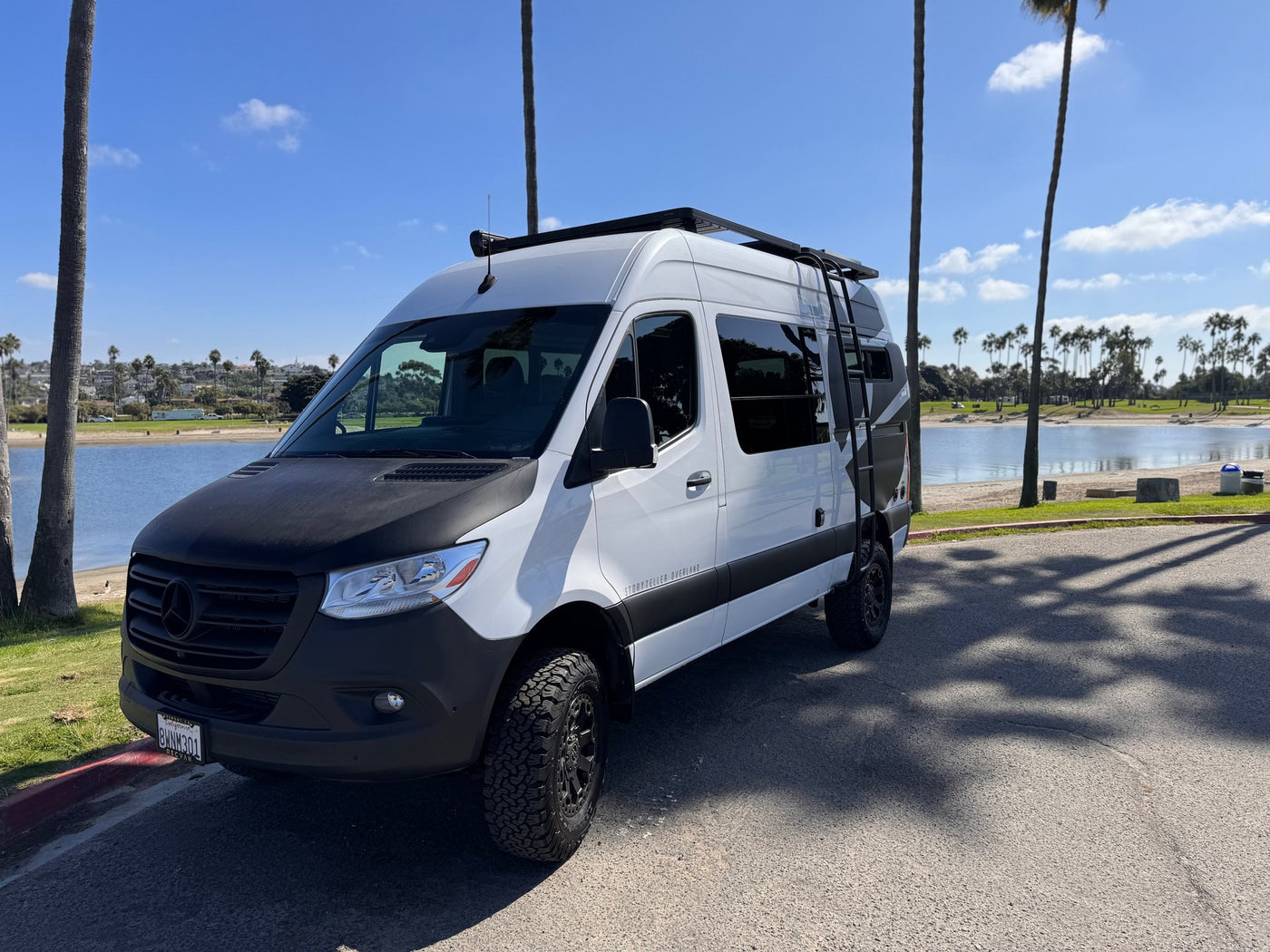 Adventure-ready Mercedes Sprinter RV rental parked by a scenic bay with palm trees, ideal for overland journeys. — photo 18